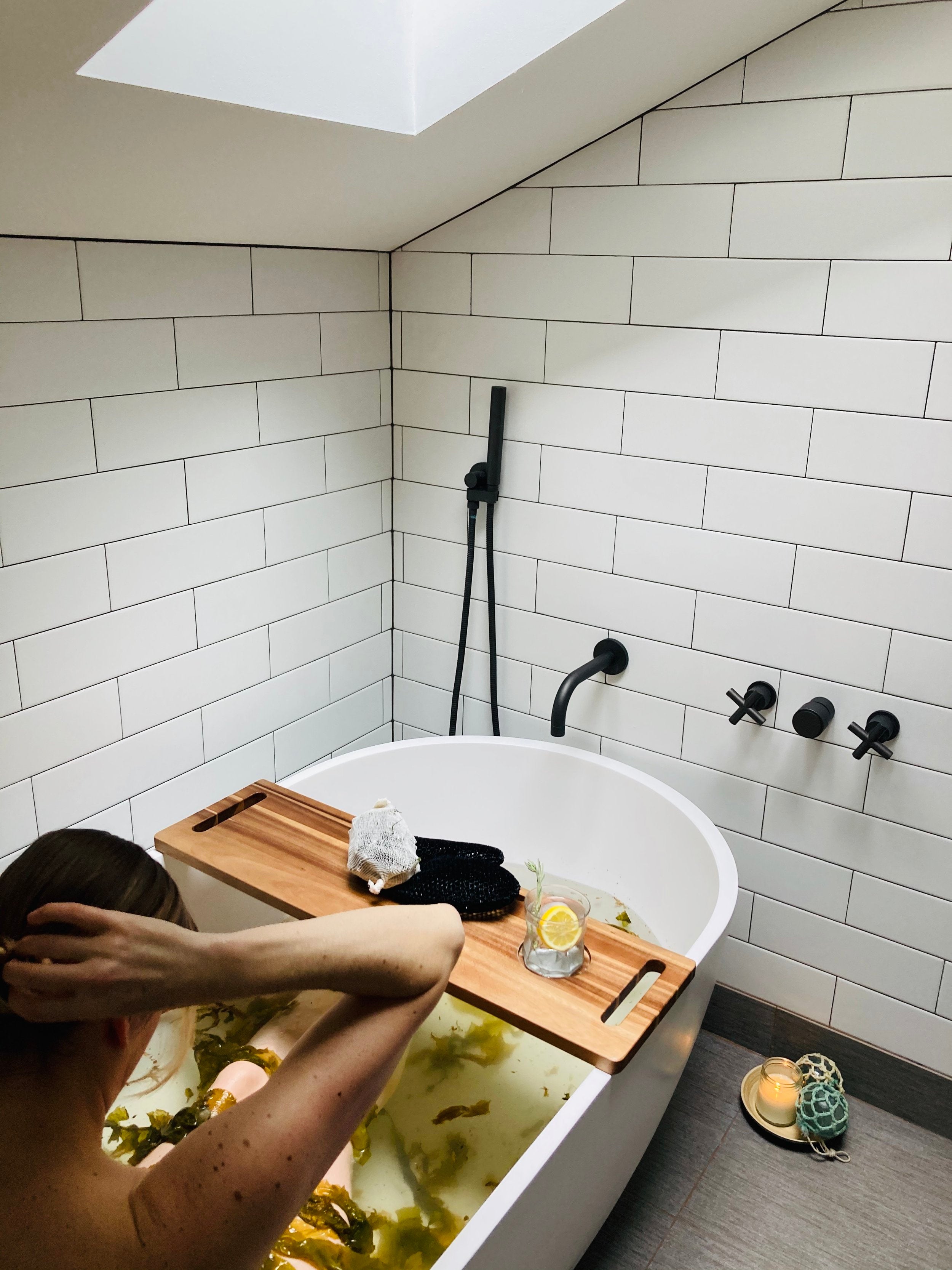 Woman enjoying a Healing Deep Sea Soak in a freestanding white bathtub of water and seaweed.