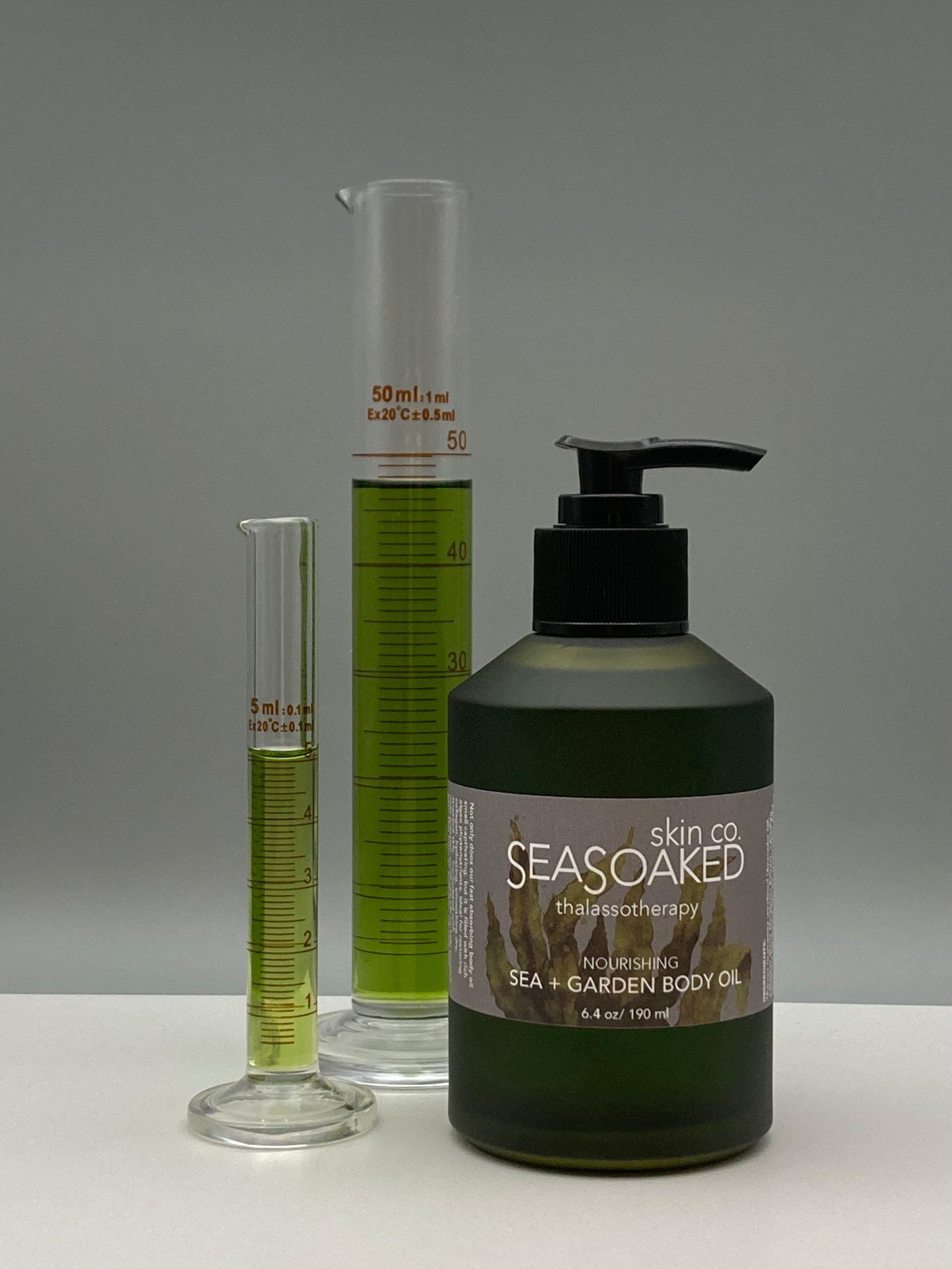 Sea Garden Body Oil pump bottle near slim beakers of same body oil.