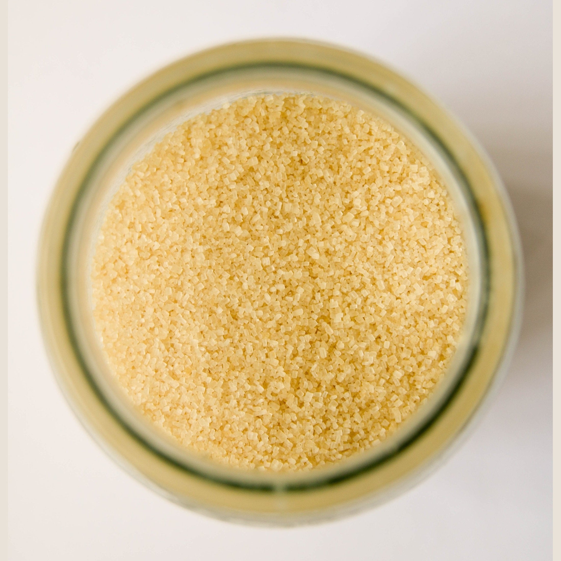 Yellowish grains of sea salt mix in a jar, as viewed from above.