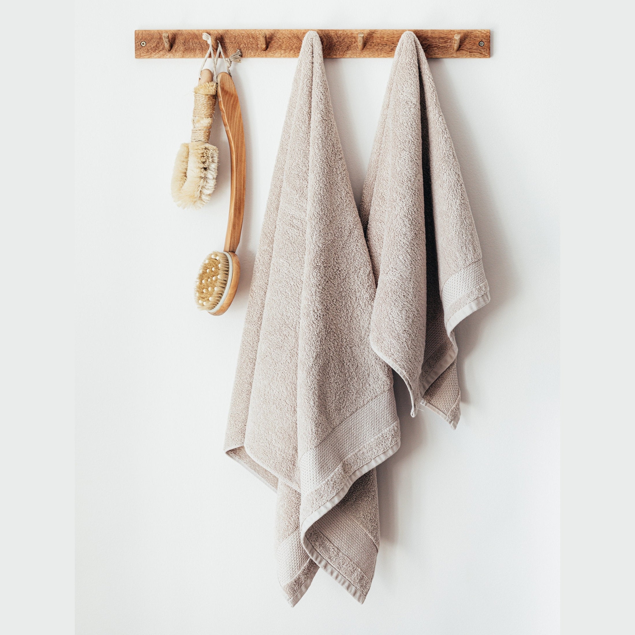 Wooden handle shower brushes with beige towels hanging from wooden peg rack.