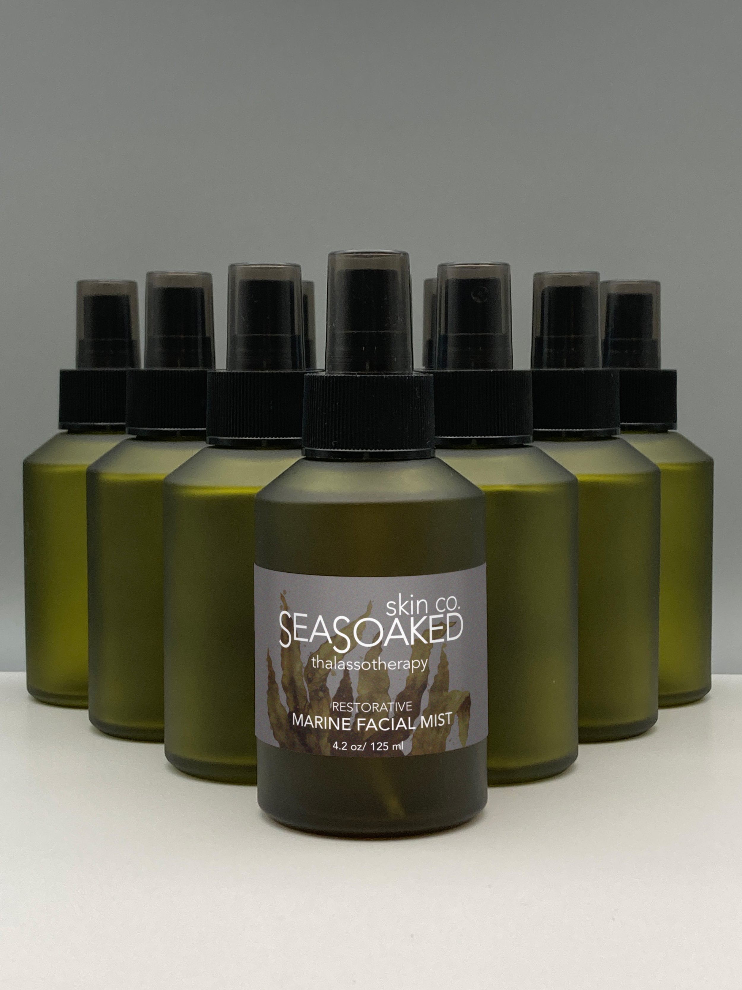 Bottle of Marine Facial Mist in front of other unlabeled frosted green bottles.